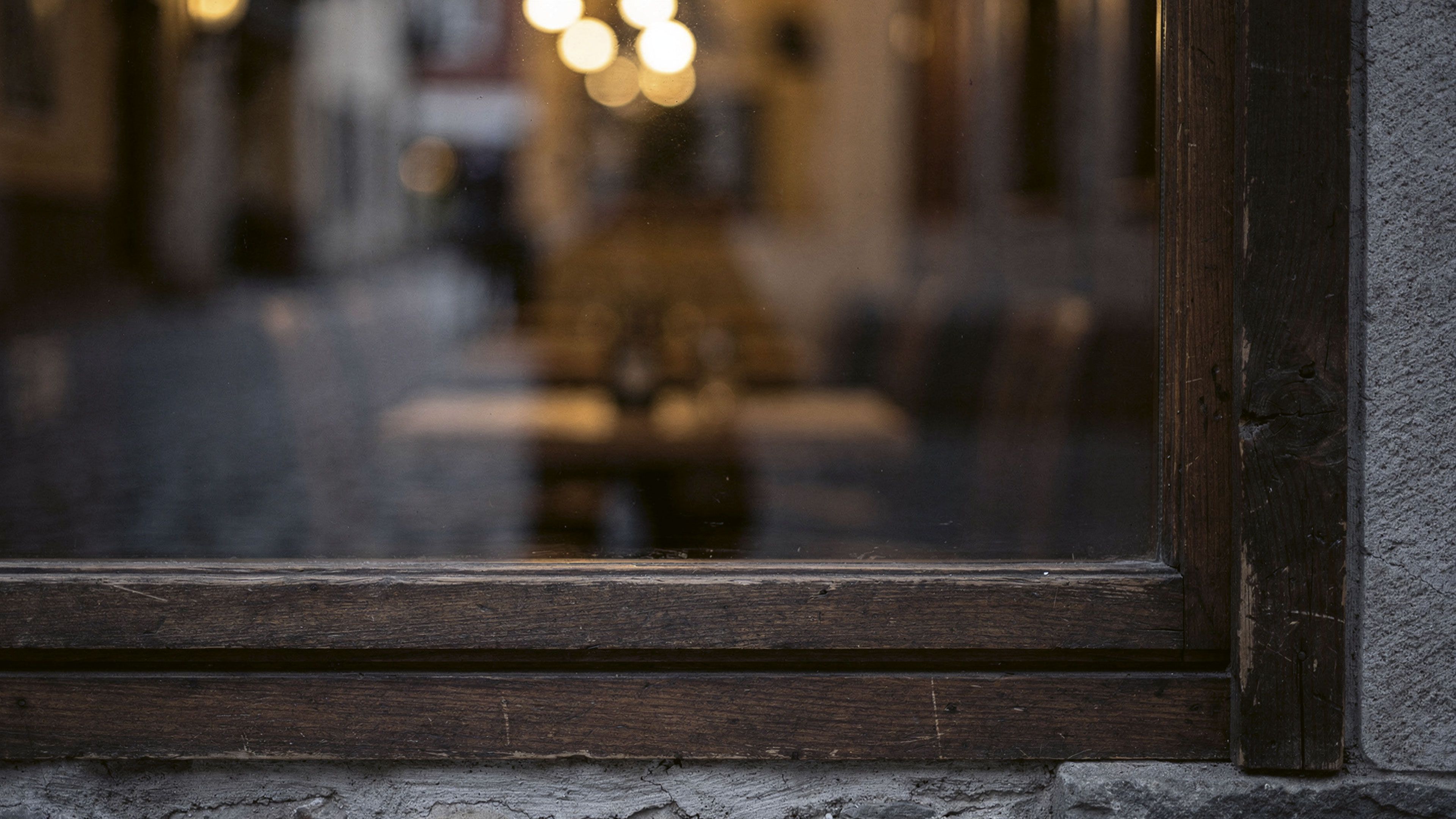 Vitrine d’un restaurant au crépuscule, dans une ruelle du vieux Monthey. Derrière la vitre, une salle tamisée aux lumières chaudes.